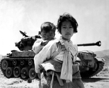 A Korean girl with her brother on her back moves wearily past a stalled tank near Haengju